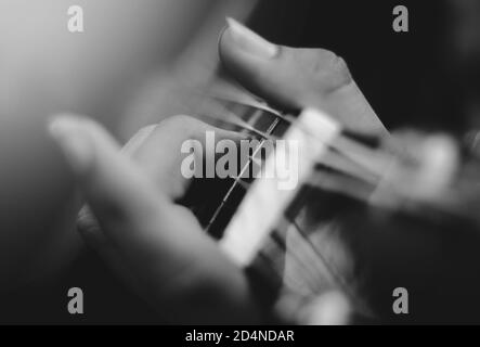 Nahaufnahme der Finger eines Mannes, der Gitarrensaiten spielt - monochrom Stockfoto