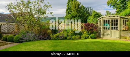 Landschaftlich schöner sonniger privater Garten (modernes Design, Sommer-Randpflanzen, Sommerhaus Schuppen, beschnittene Topiary Bälle, Rasen) - Yorkshire, England, Großbritannien. Stockfoto