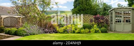 Landschaftlich schöner sonniger privater Garten (modernes Design, Sommer-Randpflanzen, Sommerhaus Schuppen, beschnittene Topiary Bälle, Rasen) - Yorkshire, England, Großbritannien. Stockfoto