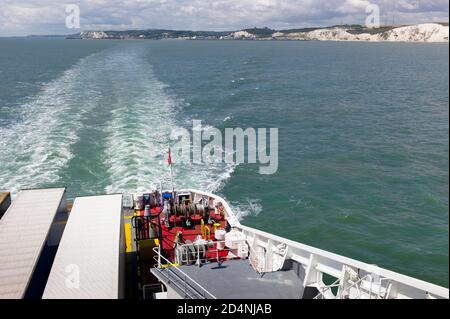 Große rote Seilrollen mit Stahlseilen auf dem Achterdeck einer Fähre mit Blick auf die Kreidefelsen von Dover. Es gibt zwei Lastwagen auf dem Deck Stockfoto