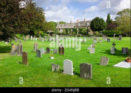 Dorf Kingham im Cotswold, Großbritannien, mit malerischen Kalksteinhäusern und Grabsteinen auf dem Friedhof Stockfoto