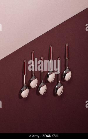 Set aus sechs Vintage Silber Dessert oder Teelöffel mit roten Emaille Details flach auf einem tiefen roten Burgund Hintergrund. Flatlay, minimalistischer Stil Stockfoto