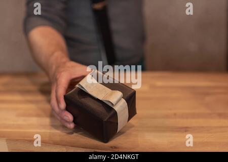 Ein Mann, der eine Geschenkbox mit schwarzem Geschenkpapier und einer Schleife hält. Gentleman gibt ein Geschenk während der Weihnachtszeit, Weihnachten oder Vatertag Stockfoto