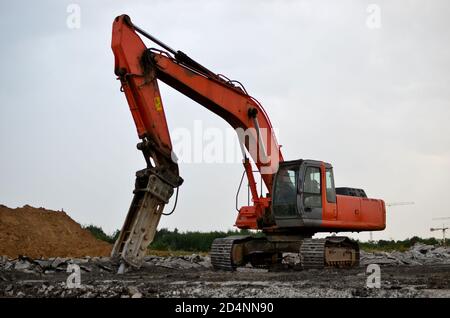 Großer Raupenbagger mit Hydraulikhammer bricht Asphalt auf einer Baustelle im Hintergrund Sonnenuntergang. Zerbrechendes Gestein und Stahlbeton. R Stockfoto