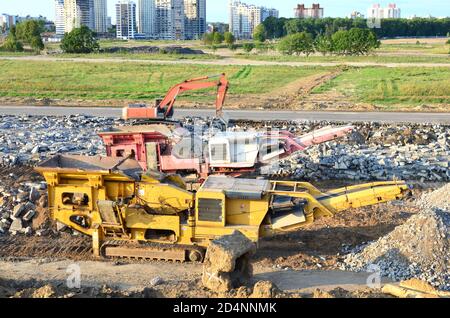 Schwerer Raupenbagger last Stein, mit alten Asphalt oder Beton Abfall in eine Mobile Backenbrecher Maschine. Die Zerkleinerung und Verarbeitung in Kies für Recycling Stockfoto