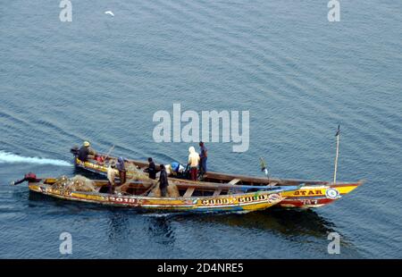 Alte hölzerne, viele farbige Fischerboote, die mit einheimischen afrikanischen Einheimischen bemannt sind, die in der Nähe von Freetown in Sierra Leone zum Fischfang gehen und Netze vorbereiten. Stockfoto