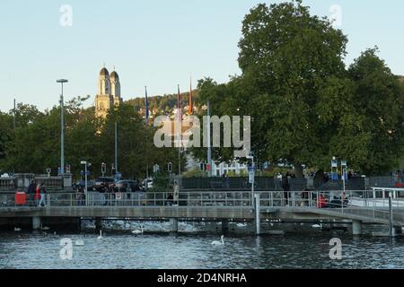 Zürichsee-Pier an einem frühen Herbstwochenende mit Grossmünster-Kirchtürmen im Hintergrund. Die Menschen gehen umher und genießen natürliche Elemente. Stockfoto