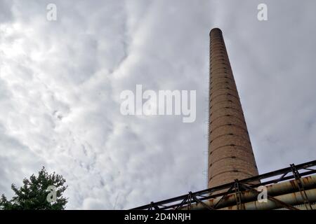 Hoher Ziegelkamin, der in einem niedrigen Winkel in einer alten Industriezone in einer Provinzstadt in Osteuropa fotografiert wurde. Der Kamin ist außer Betrieb. Stockfoto