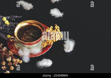 Vintage weiß rot und Gold Teetasse mit grünen Kräutern in ihm auf einem dunkelschwarzen Tisch. Freitextbereich auf der rechten Seite. Getrocknete Kamille, Lavendel Stockfoto