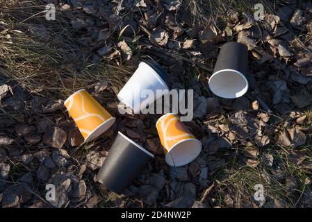 Die Leute werfen Pappkaffeetassen auf den Boden. Das Problem der Umweltverschmutzung. Stapel von verlassenen Kaffeetassen auf Gras im Park Stockfoto