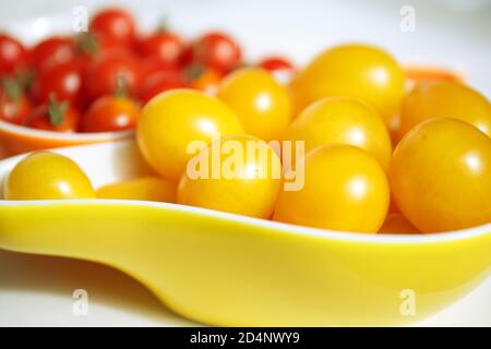 Gelbe und rote Kirschtomaten. Gelbe Kirschtomaten liegen in einer gelben Schüssel vor einem verschwommenen Hintergrund aus roten kleinen Tomaten. Herbst Kollektion von ve Stockfoto