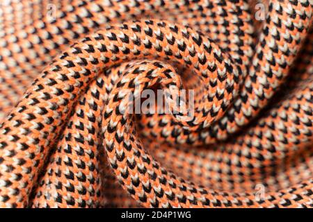 Gedrehte Falten aus synthetischem Strickgewebe mit Musterelementen aus roten, schwarzen und weißen Garnen aus nächster Nähe. Mehrfarbig gemusterte Strickstruktur. B Stockfoto