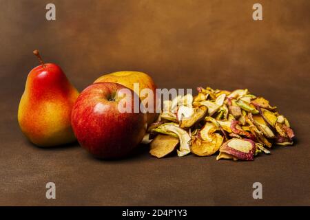 Haufen getrockneter Äpfel zusammen mit zwei ganzen Äpfeln und einer Birne. Stillleben Konzept der Herbsternte und hausgemachte Obstverarbeitung Stockfoto