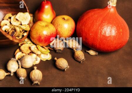Stillleben von frischen roten Kuri-Kürbis, Mohnköpfen und einem Stapel getrockneter Äpfel in einer Holzschale zusammen mit zwei ganzen Äpfeln und einer Birne. Stillleben c Stockfoto