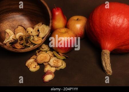 Stillleben von frischen roten Kuri-Kürbis, Mohnköpfen und einem Stapel getrockneter Äpfel in einer Holzschale zusammen mit zwei ganzen Äpfeln und einer Birne. Stillleben c Stockfoto