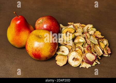 Haufen getrockneter Äpfel zusammen mit zwei ganzen Äpfeln und einer Birne. Stillleben Konzept der Herbsternte und hausgemachte Obstverarbeitung Stockfoto