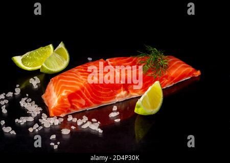 Leicht gesalzene Forelle. Frisches Fischfilet mit kulinarischen Zutaten, Kräuter und Zitrone auf schwarzem Hintergrund, Seitenansicht. Speicherplatz kopieren Stockfoto