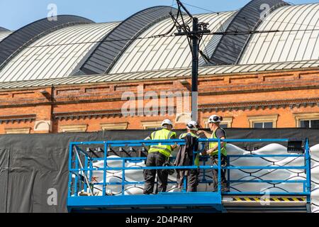 Drei Bauarbeiter auf einer Plattform Inspektion Keramikfliesen in Manchester City Center Installation, Teil der Muschelspitze Struktur. Stockfoto