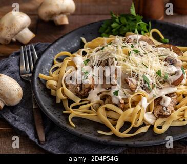 Cremiger Fettuccine alfredo mit Pilzen und zerfetztem Parmesan auf schwarzem Teller. Nahaufnahme Stockfoto