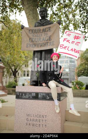 Eine Frau, die auf dem Sockel der Statue von Millicent Garrett Fawcett auf dem Parliament Square sitzt, während des marsches, in Solidarität mit den Frauen von Belarus, zur Downing Street, London. Stockfoto