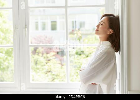 Schöne junge asiatische Frau am Fenster zu Hause Arme stehen Gekreuzte Augen geschlossen Stockfoto