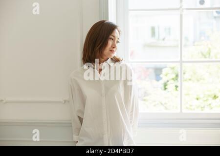 Junge asiatische Frau stehen am Fenster zu Hause glücklich und Inhalt Stockfoto