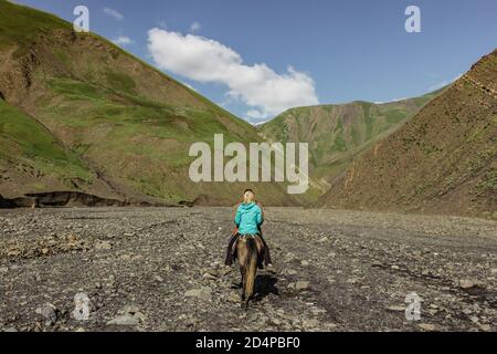 Mädchen und Mann reiten auf einem Pferd in einem Tal des Großen Kaukasus, Aserbaidschan. Reiten auf dem braunen Pferd in einem Pfad in den Hügeln. Grünes Tal, wilde Natur Stockfoto