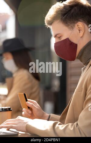Seitenansicht des jungen eleganten Geschäftsmannes in Schutzmaske Shopping Online Stockfoto