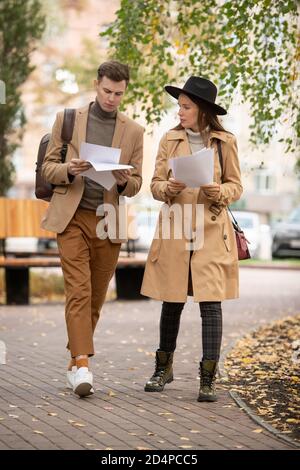 Zwei zeitgenössische Studenten in eleganter Casualwear, die durch Papiere schauen Stockfoto