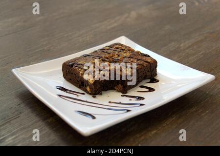 Ein Stück Brownies in einem Teller mit Schokoladensauce und gehackten Nüssen. Stockfoto