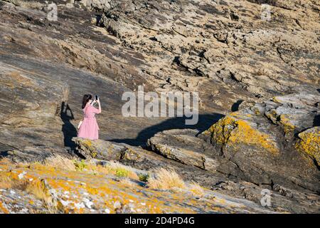 PORTONOVO, SPANIEN - 15. AUGUST 2020: Eine junge Frau macht ein Foto mit ihrem Smartphone, während sie den Sonnenuntergang auf den Felsen im Rias Baixas, Galic, genießt Stockfoto