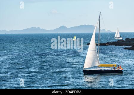 PORTONOVO, SPANIEN - 15. AUGUST 2020: Ein kleines Boot fährt in der Abenddämmerung von der Ria de Pontevedra in Galicien weg, mit den Cies-Inseln im Hintergrund. Stockfoto
