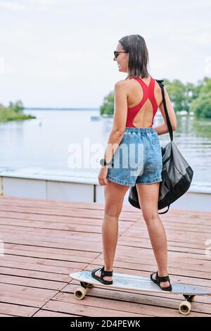 Rückansicht des Mädchens in Denim-Shorts, Sonnenbrillen und Badeanzug, die sich auf dem Skateboard bewegen Stockfoto