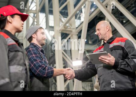 Bald reifen Vorarbeiter mit digitalen Tablet Begrüßung seiner beiden jungen Untergebene Stockfoto