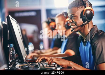 Professioneller Player. Seitenansicht eines jungen aufgeregt afrikanischen Kerl, männliche Cybersport-Gamer mit Kopfhörern spielen Online-Videospiele, während die Teilnahme mit Team in eSport Turnier Stockfoto