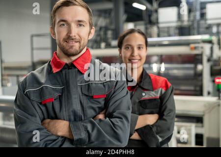 Glücklicher junger bärtiger männlicher Leiter des Arbeitsteams, der gegen die Frau steht Kollege Stockfoto
