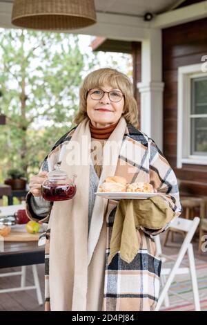 Glücklich reif blonde Frau in karierte Wolle kariert Plaid halten gewickelt Snack Stockfoto