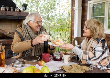 Glücklicher Mann im Alter in warmer Casualwear unter frischen hausgemachten Brötchen Von Platte Stockfoto