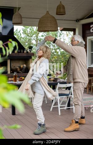 Happy Senior paar in warmen stilvollen Casualwear tanzen auf Holz Etage der Terrasse Stockfoto