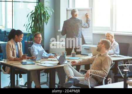Reifer Mann, der etwas an der weißen Tafel schreibt, ein Brainstorming-Treffen mit dem Team im modernen Büro oder Coworking Space hat. Geschäftsleuten Stockfoto