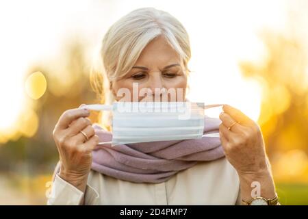 Ältere Frau, die im Freien eine Schutzmaske aufsetzt Stockfoto