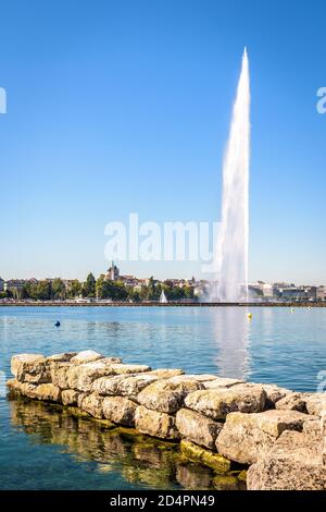 Die Stadt und Bucht von Genf, Schweiz, von einem Steinsteg aus gesehen von einem sonnigen Sommermorgen mit der Kathedrale und dem Jet d'Eau, der 140 Meter hohen Waa Stockfoto