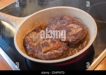 Fleischkonzept. Zwei Schweinelenden Koteletts in Steinpfanne mit Öl auf Herd gebraten. Gut gemacht braune Steaks auf Scheiben bereit serviert werden. Verwischen Sie den Hintergrund, Nahaufnahme Stockfoto