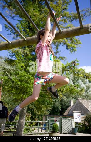 Junges Mädchen schwingt über Affenriegel im Spielpark Stockfoto