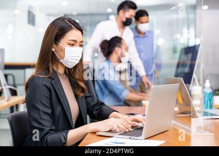 Portrait der asiatischen Büroangestellte Geschäftsfrau tragen Schutzmaske Arbeiten Sie in einem neuen normalen Büro mit interracial Team im Hintergrund Als soziale dist Stockfoto