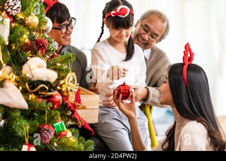 Mehrgenerationenübergreifende asiatische Familie, die einen Weihnachtsbaum schmückt. Mama Papa Tochter Mädchen und Großvater schmücken den Weihnachtsbaum Vorbereitung für die Saison begrüßen Stockfoto