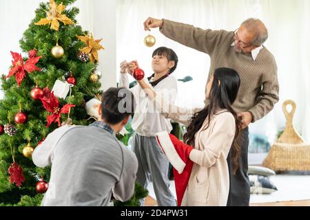 Mehrgenerationenübergreifende asiatische Familie, die einen Weihnachtsbaum schmückt. Mama Papa Tochter Mädchen und Großvater schmücken den Weihnachtsbaum Vorbereitung für die Saison begrüßen Stockfoto