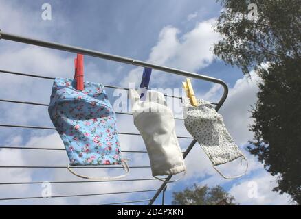 Drei wiederverwendbare Tuch Gesichtsmasken trocknen an einer Wäscheleine im Freien an einem sonnigen Tag. COVID 19 Prävention, umweltfreundliches Konzept. Stockfoto