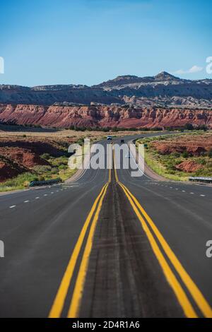 Klassischer Panoramablick auf eine endlose gerade Straße, die durch die karge Landschaft des amerikanischen Südwestens führt. Stockfoto