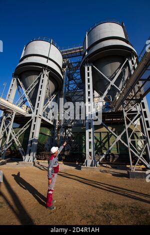 Region Aktobi/Kasachstan - Mai 04 2019: Phosphatdüngeanlage. Bahnhopper Auto Terminal. Düngemittel Lader und Zug. Arbeiter in weißem Helm Stockfoto